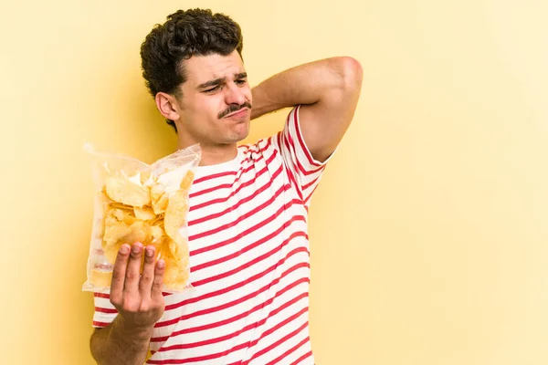 Young Caucasian Man Holding Bag Chips Isolated Yellow Background Touching — Stockfoto
