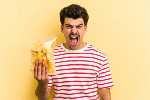 Young Caucasian Man Holding Bag Chips Isolated Yellow Background Screaming — Stock fotografie