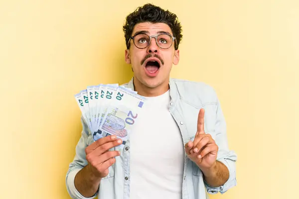 Young Caucasian Man Holding Banknotes Isolated Yellow Background Pointing Upside — Stock fotografie