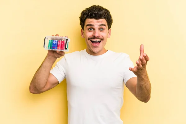 Young Caucasian Man Holding Batteries Isolated Yellow Background Receiving Pleasant — ストック写真