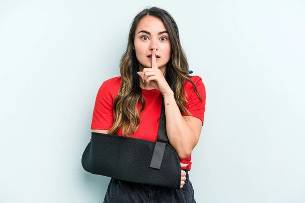 Young caucasian woman with broke hand isolated on blue background keeping a secret or asking for silence.