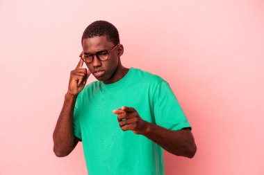 Genç Afrikalı Amerikalı bir adam pembe arka planda izole edilmiş. Parmağıyla tapınağı işaret ediyor, düşünüyor ve bir göreve odaklanıyor..