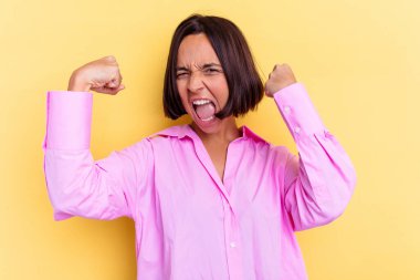 Sarı arka planda izole edilmiş genç bir ırk kadını güçlü bir jest yapıyor, kadınsı gücün sembolü.