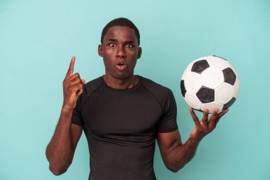 Genç Afrikalı Amerikalı bir adam mavi arka planda izole bir şekilde futbol oynuyor. Harika bir fikri var, yaratıcılık kavramı..
