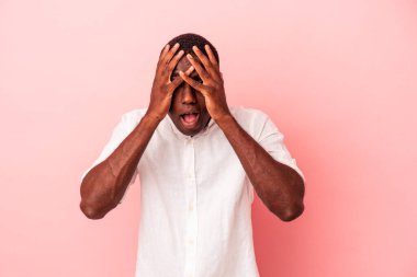 Genç Afrikalı Amerikalı bir adam pembe arka planda izole edilmiş. Yüzünün yarısını palmiye ile örterek eğleniyor..