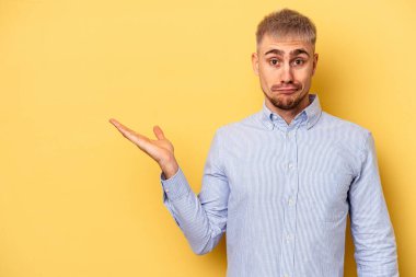 Sarı arka planda izole edilmiş genç beyaz bir adam bir palmiye üzerinde fotokopi alanı gösteriyor ve belinde başka bir el tutuyor..