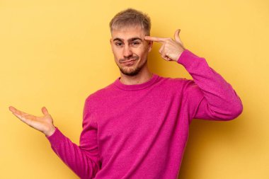 Genç beyaz adam sarı arka planda izole edilmiş ve elinde bir ürün var..