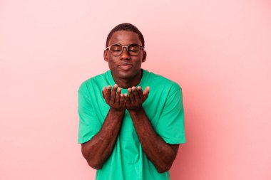 Genç Afro-Amerikalı adam pembe arka planda izole edilmiş dudaklar kıvrılmış ve avuç içi tutarak hava öpücüğü gönderiyor..