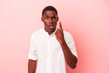 Genç Afro-Amerikalı, pembe arka planda izole edilmiş, ağzı açık, üst tarafı işaret ediyor..