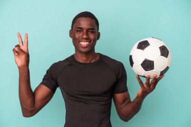 Futbol oynayan genç Afrikalı Amerikalı adam mavi arka planda izole edilmiş neşeli ve kaygısız parmaklarıyla barış sembolü gösteriyor..