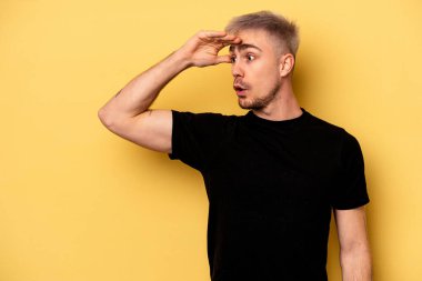 Kafkasyalı genç adam sarı arka planda izole edilmiş, uzaklara bakıyor ve elini alnına koyuyor..