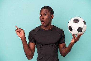 Mavi arka planda izole bir şekilde futbol oynayan genç bir Afro-Amerikan.