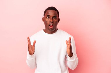 Genç Afrikalı Amerikalı bir adam pembe arka planda izole edilmiş zaferi ya da başarıyı kutluyor, şaşırmış ve şok olmuş..