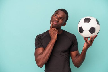 Mavi arka planda izole bir şekilde futbol oynayan genç Afrikalı Amerikalı şüpheli ve şüpheci bir ifadeyle yana bakıyor..