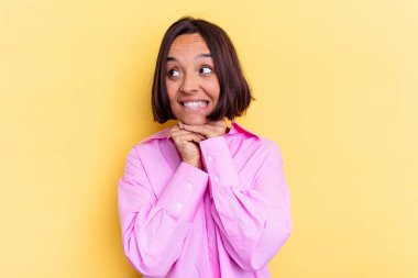 Sarı arka planda izole edilmiş genç melez kadın ellerini çenesinin altında tutuyor, mutlu bir şekilde yana bakıyor..