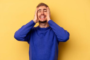 Sarı arka planda izole edilmiş genç beyaz adam ellerini başının üstünde tutarak neşe içinde gülüyor. Mutluluk kavramı.