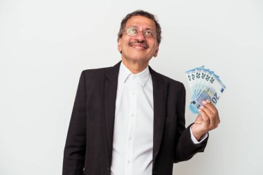 Middle aged indian business man holding bills isolated on white background dreaming of achieving goals and purposes