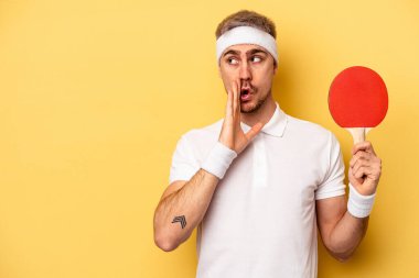 Young caucasian man holding ping pong rackets isolated on yellow background is saying a secret hot braking news and looking aside
