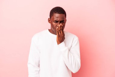 Genç Afrikalı Amerikalı bir adam pembe arka planda izole edilmiş esniyor. Ağzı eliyle kapatan yorgun bir jest yapıyor..