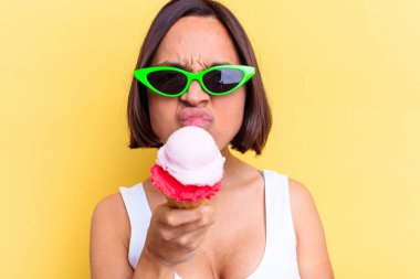 Sarı arka planda izole edilmiş dondurma tutan melez bir kadın.