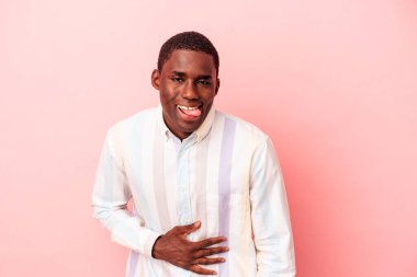 Pembe arka planda izole edilmiş genç Afrikalı Amerikalı adam karnına dokunuyor, nazikçe gülümsüyor, yemek yiyor ve tatmin oluyor..