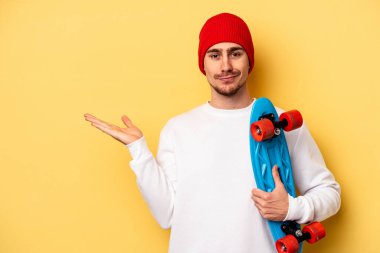 Young skater caucasian man isolated on yellow background showing a copy space on a palm and holding another hand on waist.