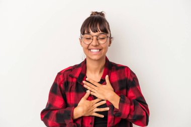 Beyaz arka planda izole edilmiş genç bir ırk kadını mutlu bir şekilde gülüyor ve ellerini karnının üstünde tutarak eğleniyor..