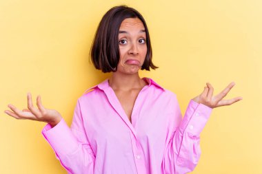 Sarı arka planda izole edilmiş genç melez bir kadın sorgulama sırasında omuz silkiyor ve şüphe duyuyor..