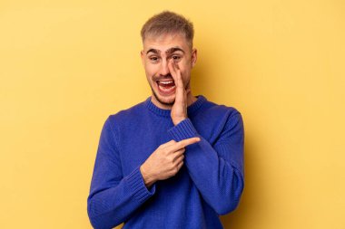 Sarı arka planda izole edilmiş genç beyaz bir adam bir dedikodu söylüyor, bir haber sunuyor..