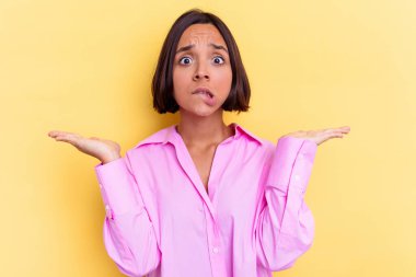 Sarı arka planda izole edilmiş genç melez bir kadın. Kafası karışmış ve omuz silkiyor. Kopya alanını tutmak için..