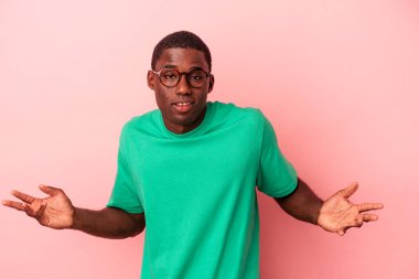 Genç Afrikalı Amerikalı, pembe arka planda izole edilmiş. Sorgulama sırasında omuz silkiyor ve şüphe ediyor..