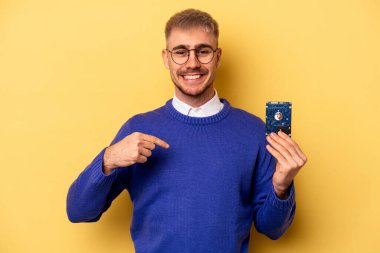 Young computer man isolated on yellow background person pointing by hand to a shirt copy space, proud and confident