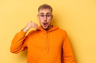 Sarı arka planda izole edilmiş genç beyaz bir adam bir şeye gülüyor, ağızlarını ellerle kapatıyor..