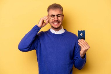 Young computer man isolated on yellow background covering ears with hands.