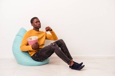 Genç Afrikalı Amerikalı bir adam beyaz arka planda izole edilmiş patlamış mısır yiyor. Sevimsiz bir jest yapıyor. Anlaşmazlık konsepti.