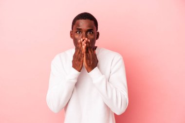 Genç Afrikalı Amerikalı bir adam pembe arka planda izole edilmiş. Şok olmuş, ağzı ellerle kaplanmış, yeni bir şey keşfetmeye hevesli..