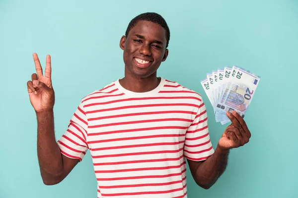 Молодой Афроамериканец Держащий Банкноты Синем Фоне Радостный Беззаботный Показывающий Символ — стоковое фото