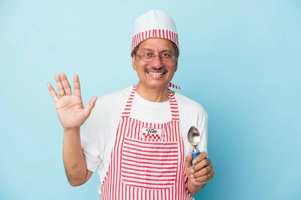 Senior indian ice cream man holding a scoop isolated on blue background smiling cheerful showing number five with fingers.