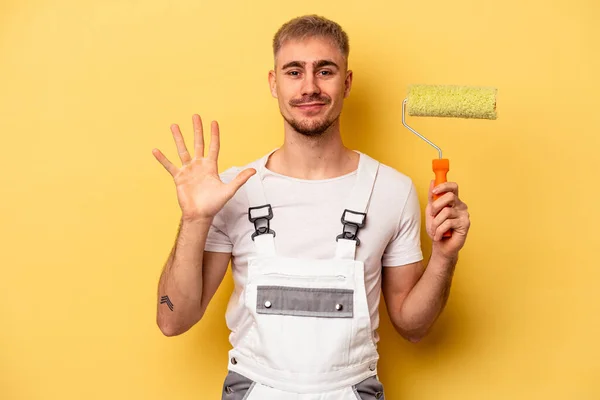 Young painter man isolated on yellow background smiling cheerful showing number five with fingers.