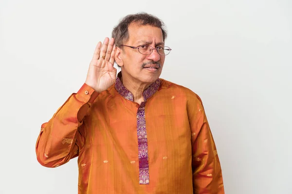 Senior indian man wearing a Indian costume isolated on white background trying to listening a gossip.