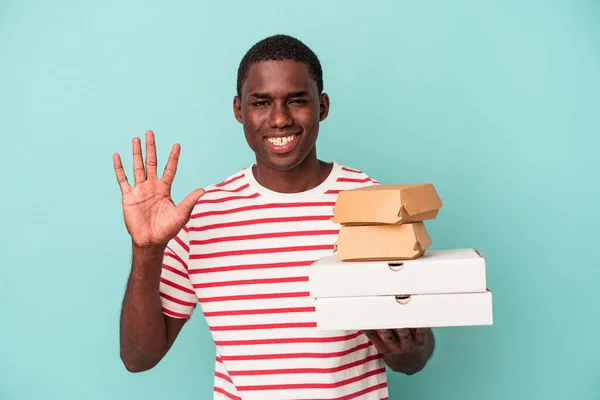 Mladý Afroameričan Drží Pizzy Hamburgery Izolované Modrém Pozadí Veselým Úsměvem — Stock fotografie