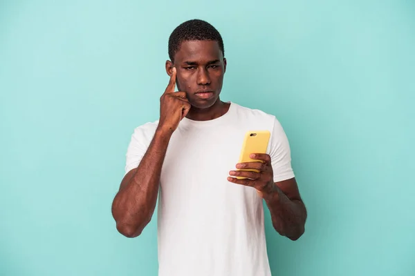 年轻的非裔美国人拿着一部蓝色背景的手机 手拿着手指 思考着 专心致志地做着一件事 — 图库照片