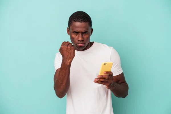 年轻的非裔美国人拿着一部蓝色背景的手机 对着摄像机 表情咄咄逼人 — 图库照片