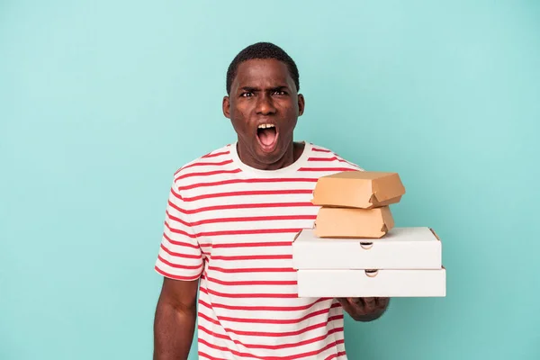 Mladý Afroameričan Drží Pizzy Hamburgery Izolované Modrém Pozadí Křičí Velmi — Stock fotografie
