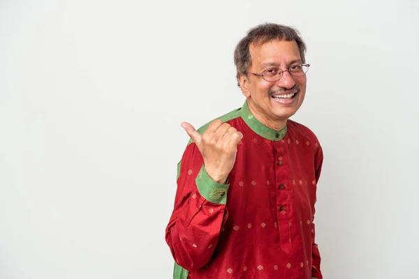 Senior indian man wearing a Indian costume isolated on white background points with thumb finger away, laughing and carefree.