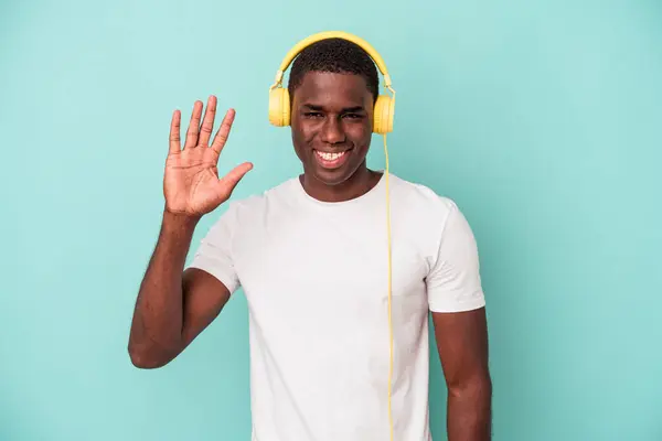 若いですアフリカ系アメリカ人男性リスニング音楽に隔離された上に青の背景笑顔陽気なショー番号5とともに指 — ストック写真
