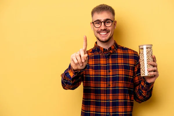 Young Caucasian Man Holding Chickpeas Isolated Yellow Background Showing Number — Stock fotografie