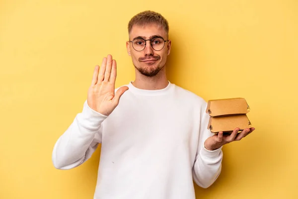 Young Caucasian Man Holding Burger Isolated Yellow Background Standing Outstretched — ストック写真