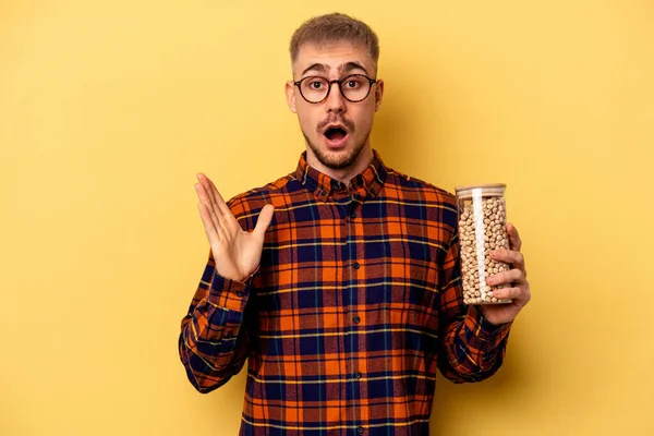 Young Caucasian Man Holding Chickpeas Isolated Yellow Background Surprised Shocked — Stockfoto