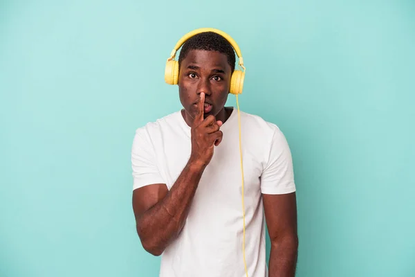 Joven Afroamericano Escuchando Música Aislada Sobre Fondo Azul Guardando Secreto —  Fotos de Stock
